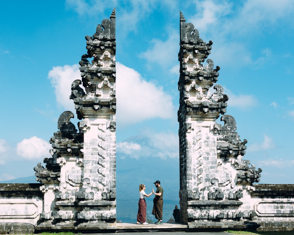 Lempuyang Temple, the temple is known as "Gate of Heaven" in Bali, Indonesia. A couple is standing and holding hands in the gateway between the temples pillars.