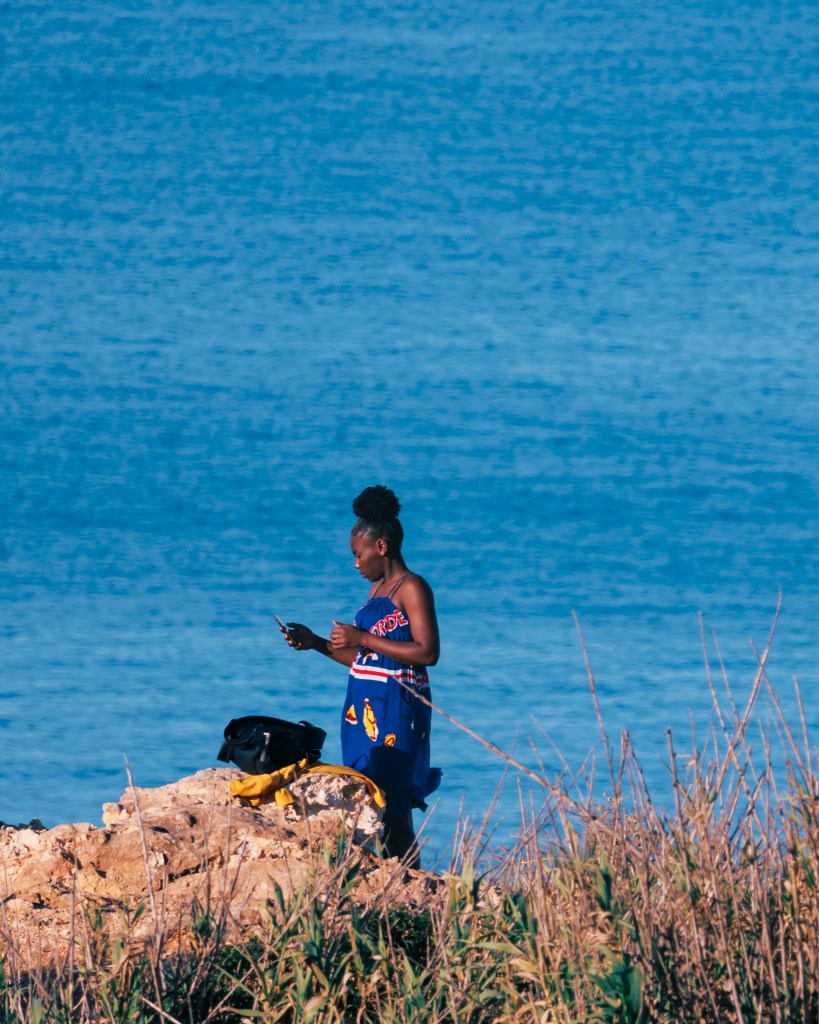 Woman standing on a cliff in Sagres, Algarve, Portugal one april morning after sunrise checking how her selfies turned out in her phone