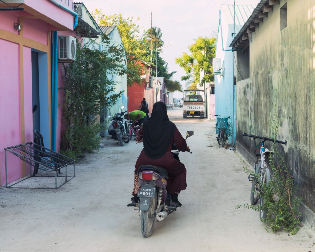 Maldivian woman driving her scooter on the narrow streets of Thulusdoo