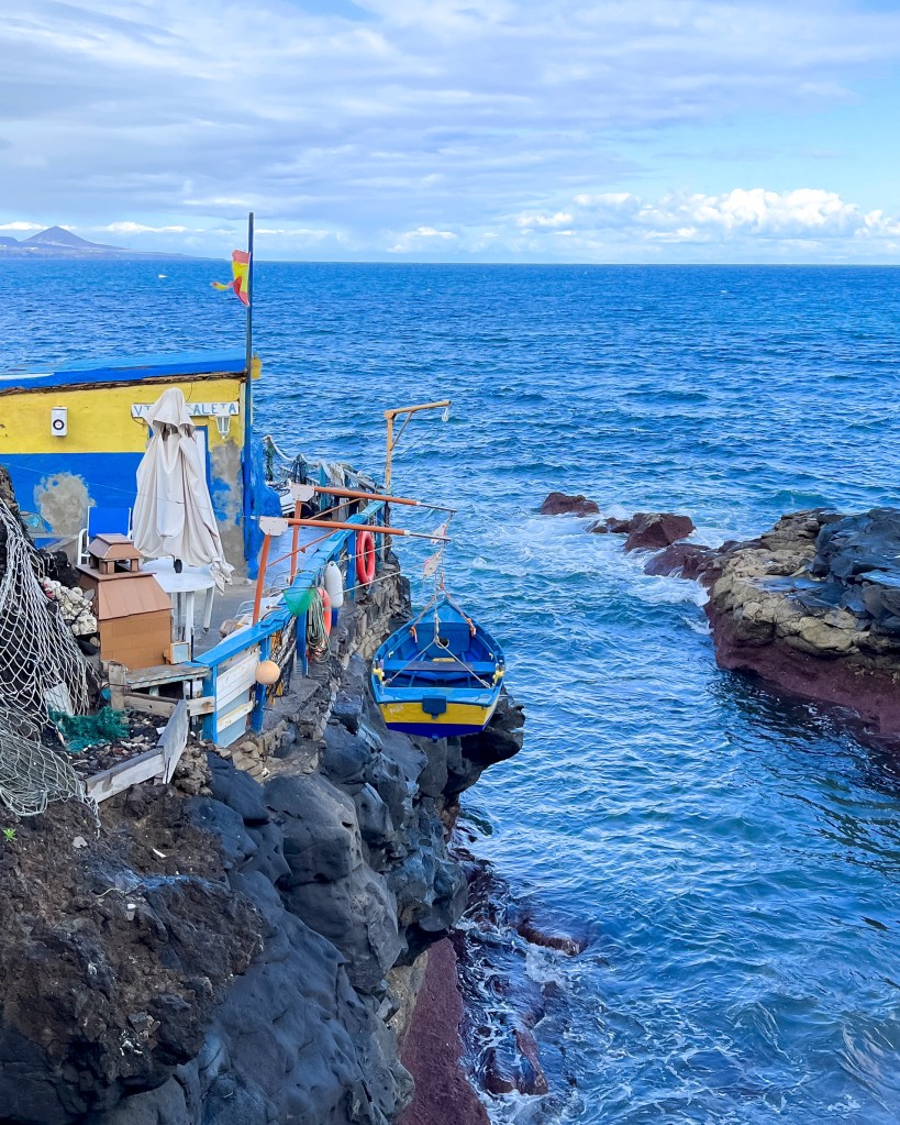 Blue and yellow fishing boat hanging beside a blue and yellow small house on the cliffs of Las Canteras just outside Las Palmas in Gran Canaria, February 2023