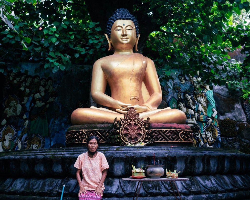 Balinese woman cleaning the temple grounds at Brahmavihara Arama temple close to Lovina north Bali sitting next to a statue of the Buddha
